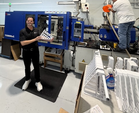 Josh holding a newly molded XpandiShelf bracket beside an injection-molding machine